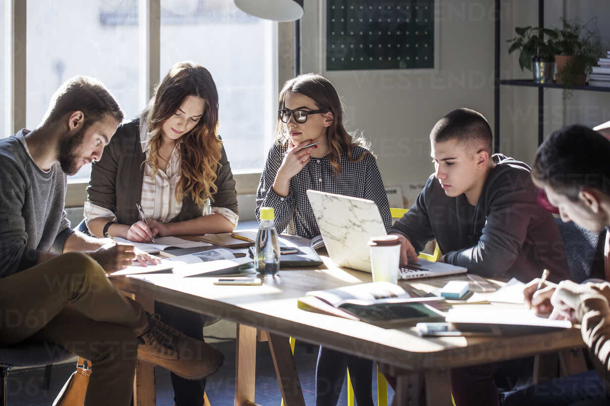 College students studying while sitting at table by window in classroom